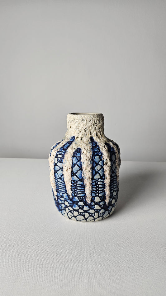 Ceramic vase with textured surface and blue patterns on a gray background
